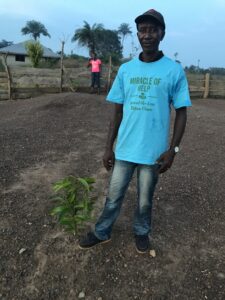 Jusu Jabbie, head man of the village stands over a young sapling